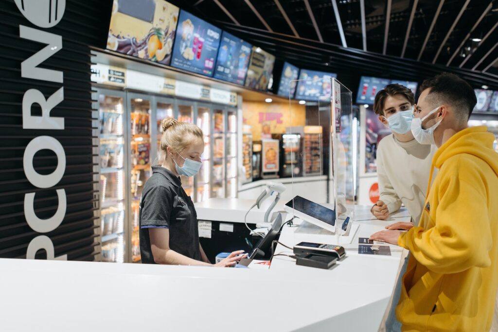men use credit card to purchase from a cashier at a store while wearing masks